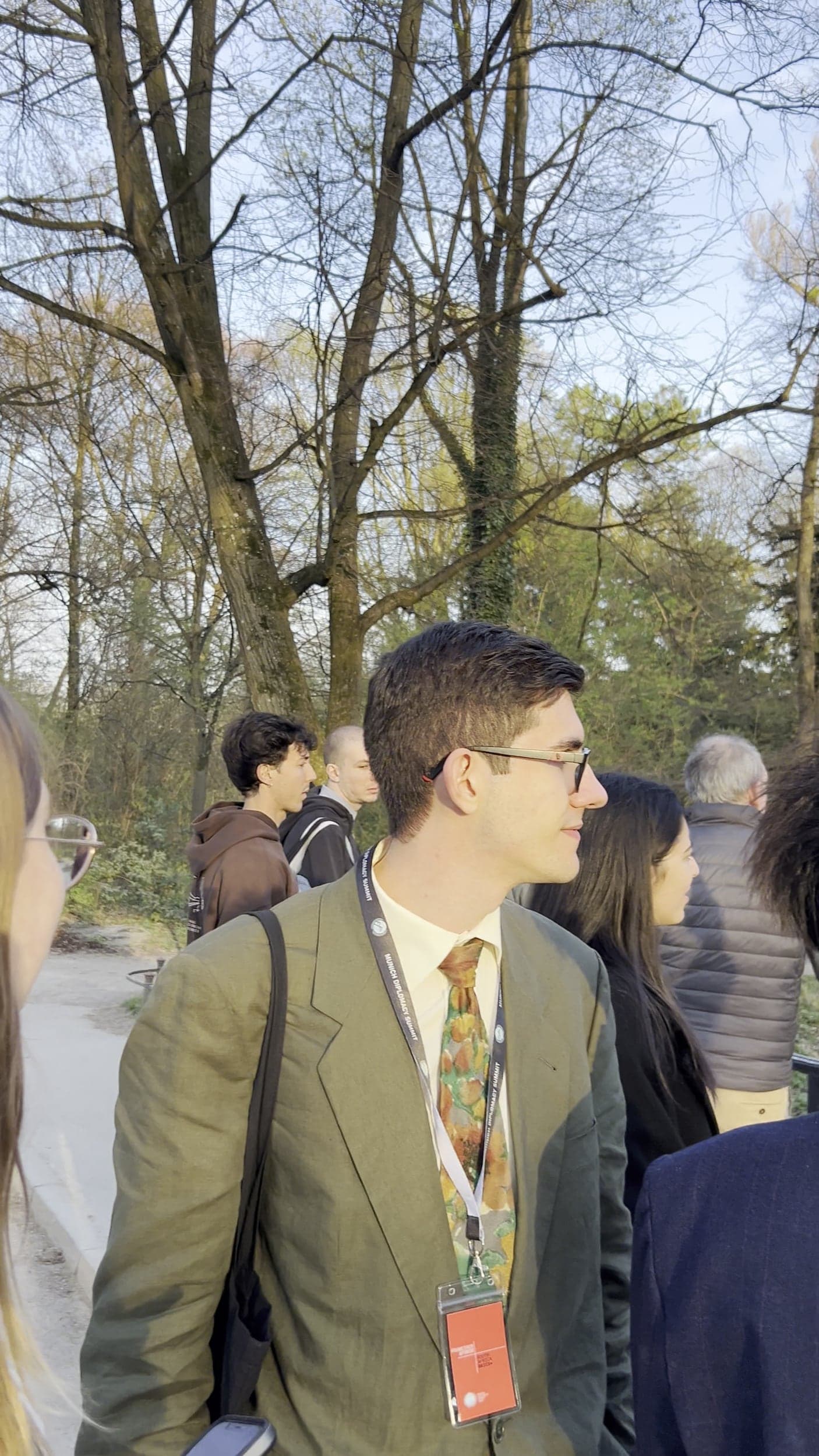 A delegate in a green suit with a conference badge on a walk through a park